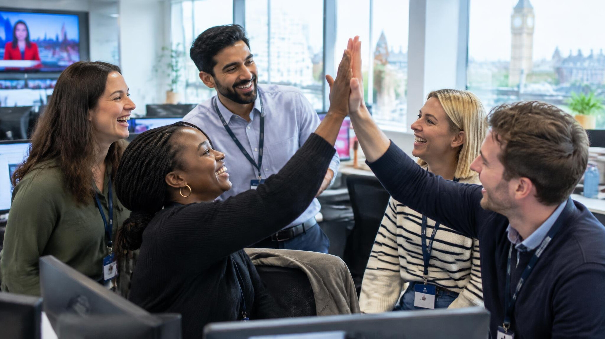 Diverse newsroom team celebrating with a high five in an office
